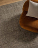 An ochre armchair on a textural slate toned charcoal floor rug with a textural loop piling in a durable wool blend. 