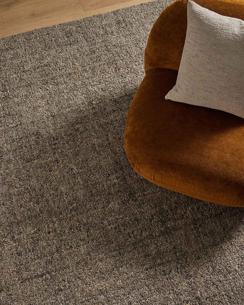 An ochre armchair on a textural slate toned charcoal floor rug with a textural loop piling in a durable wool blend. 