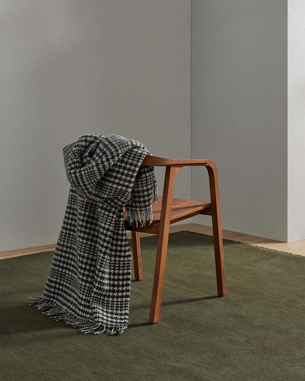 A houndstooth throw blanket in sophisticated black and white with fringed edging and 100% wool, draped over the back of a chair. 