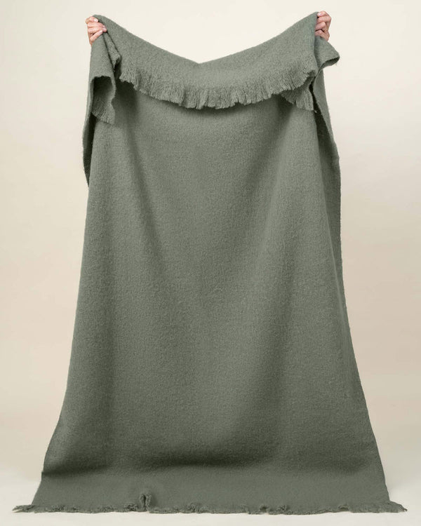 A full image of the Hyde throw blanket, held up to see the soft green shade and generous sizing. 