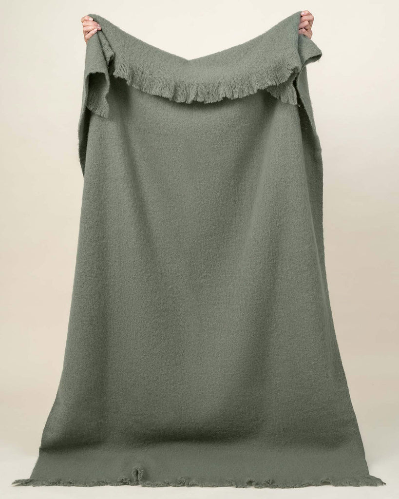 A full image of the Hyde throw blanket, held up to see the soft green shade and generous sizing. 