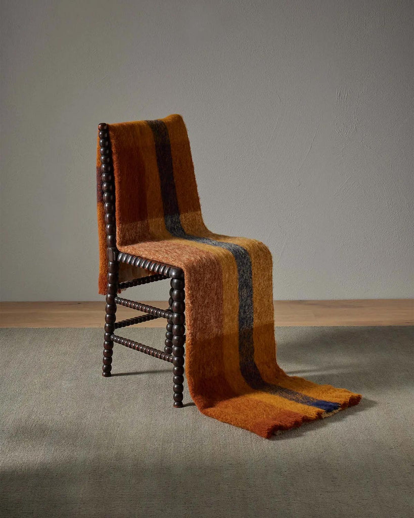 A stunning orange and brown check throw blanket with a stripe of blue and fringed edges, draped over a chair. 