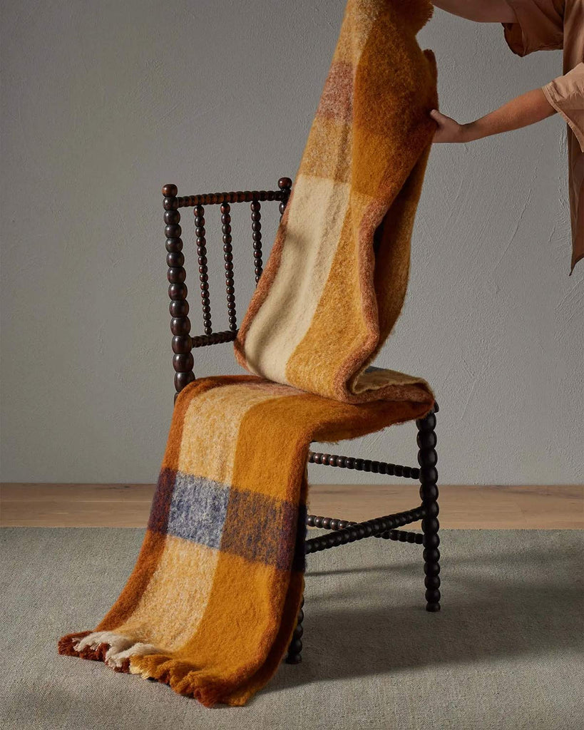 An orange and brown check throw blanket in a wool blend being draped over a chair. 