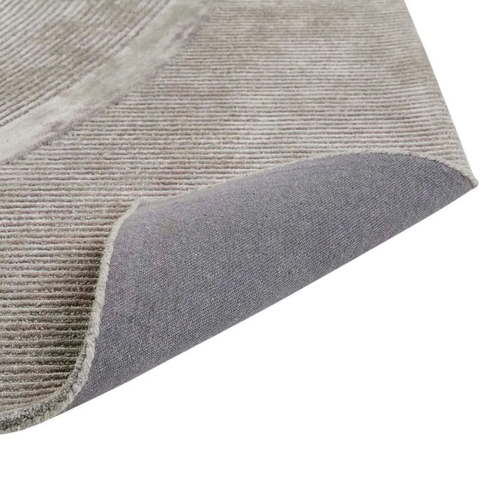 A grey wool blend floor rug feturing a circular pattern design, folded to reveal underneath