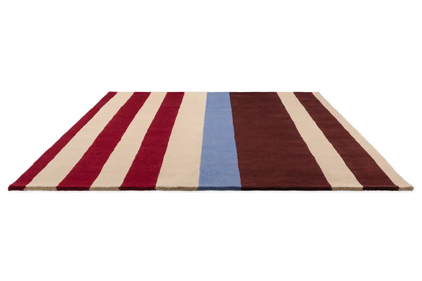 Perspective view of the Marimekko Ralli wool floor rug in striking red, maroon, cream and blue stripes