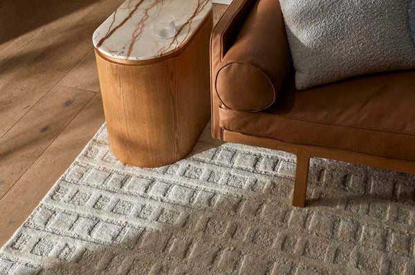 A creamy white wool-blend floor rug featuring an abstract horizontal pattern , seen under a couch leg and coffee table