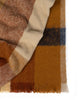 A folded throw blanket in shades of orange cream and brown, with fringed edges. 