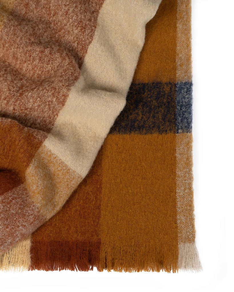 A folded throw blanket in shades of orange cream and brown, with fringed edges. 