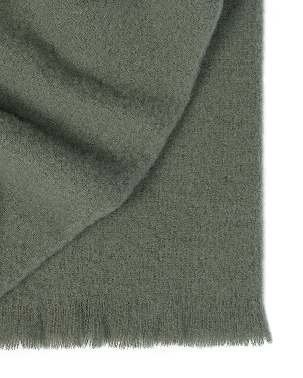 A folded soft wool blend throw blanket, with fringed edges, in a delicate shade of muted green. 