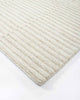 A corner image of the 100% wool floor rug by Baya, with a creamy linear pattern made with cut and looped pile. 