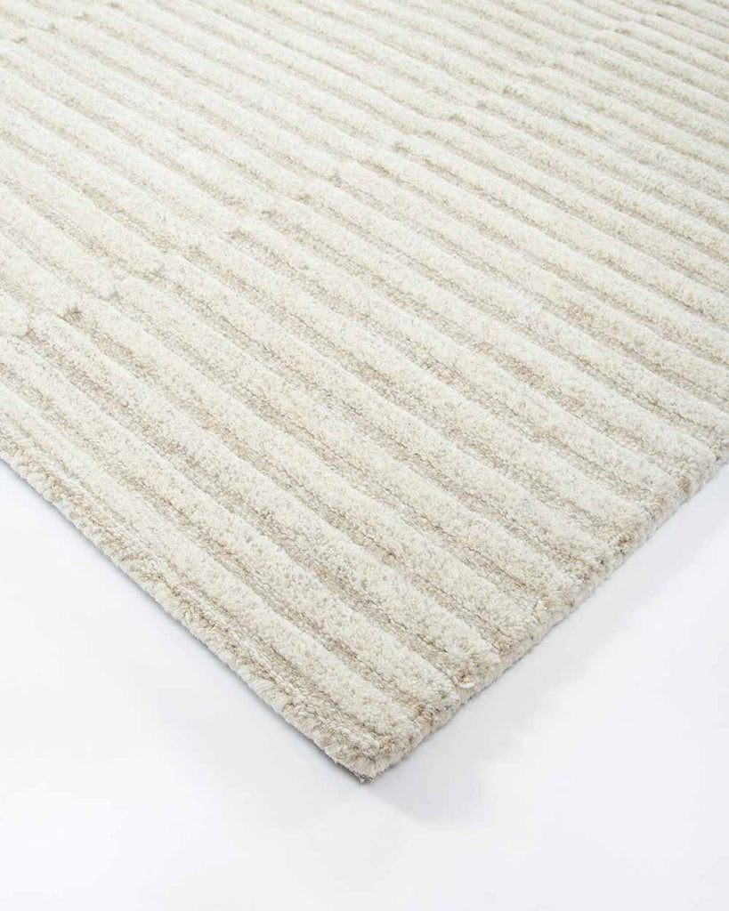 A corner image of the 100% wool floor rug by Baya, with a creamy linear pattern made with cut and looped pile. 