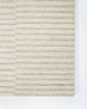 A corner image from above of the 100% wool floor rug by Baya, with a creamy linear pattern made with cut and looped pile. 