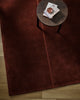 Baya Bastion NZ wool floor rug in Claret, overhead view beneath a small round side table with books, on a timber floor.