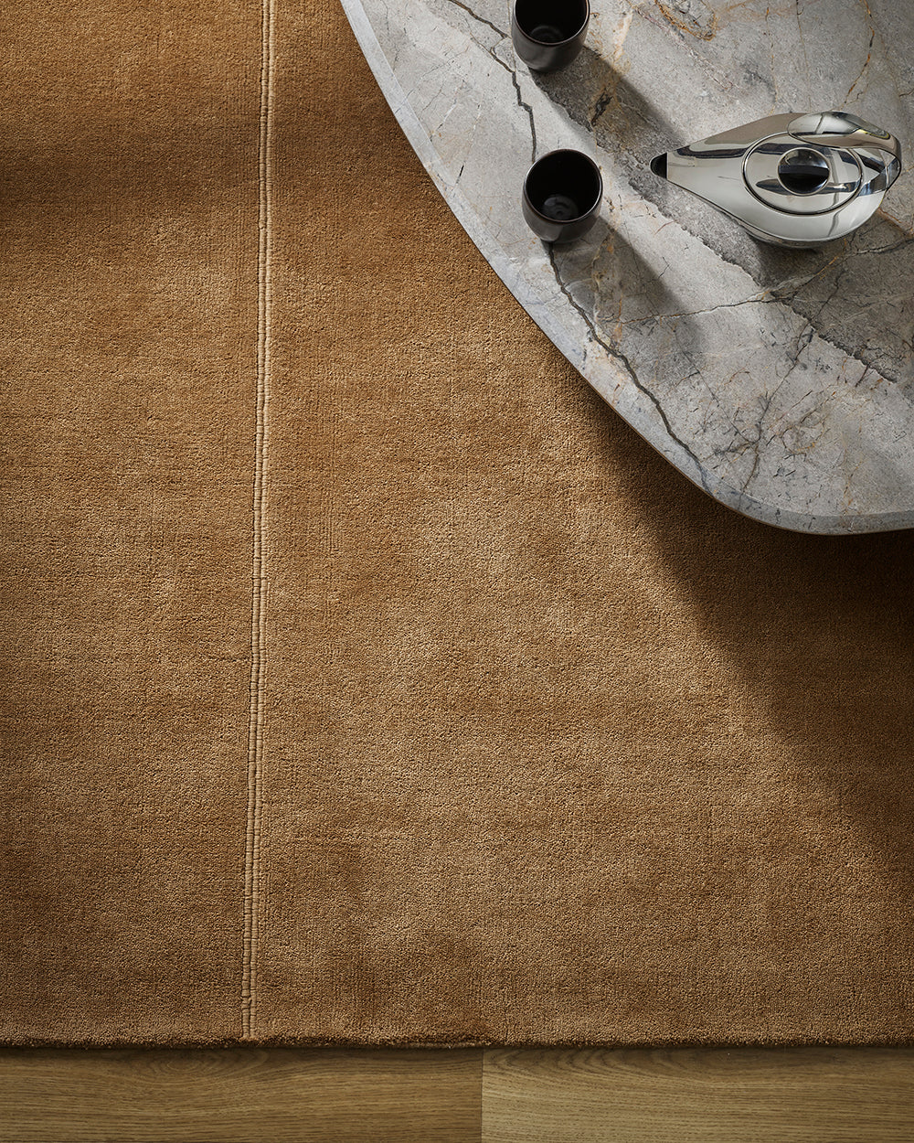 Baya Bastion NZ wool floor rug in Hazelnut, overhead view beneath a marble coffee table with a teapot and cups, on a timber floor.