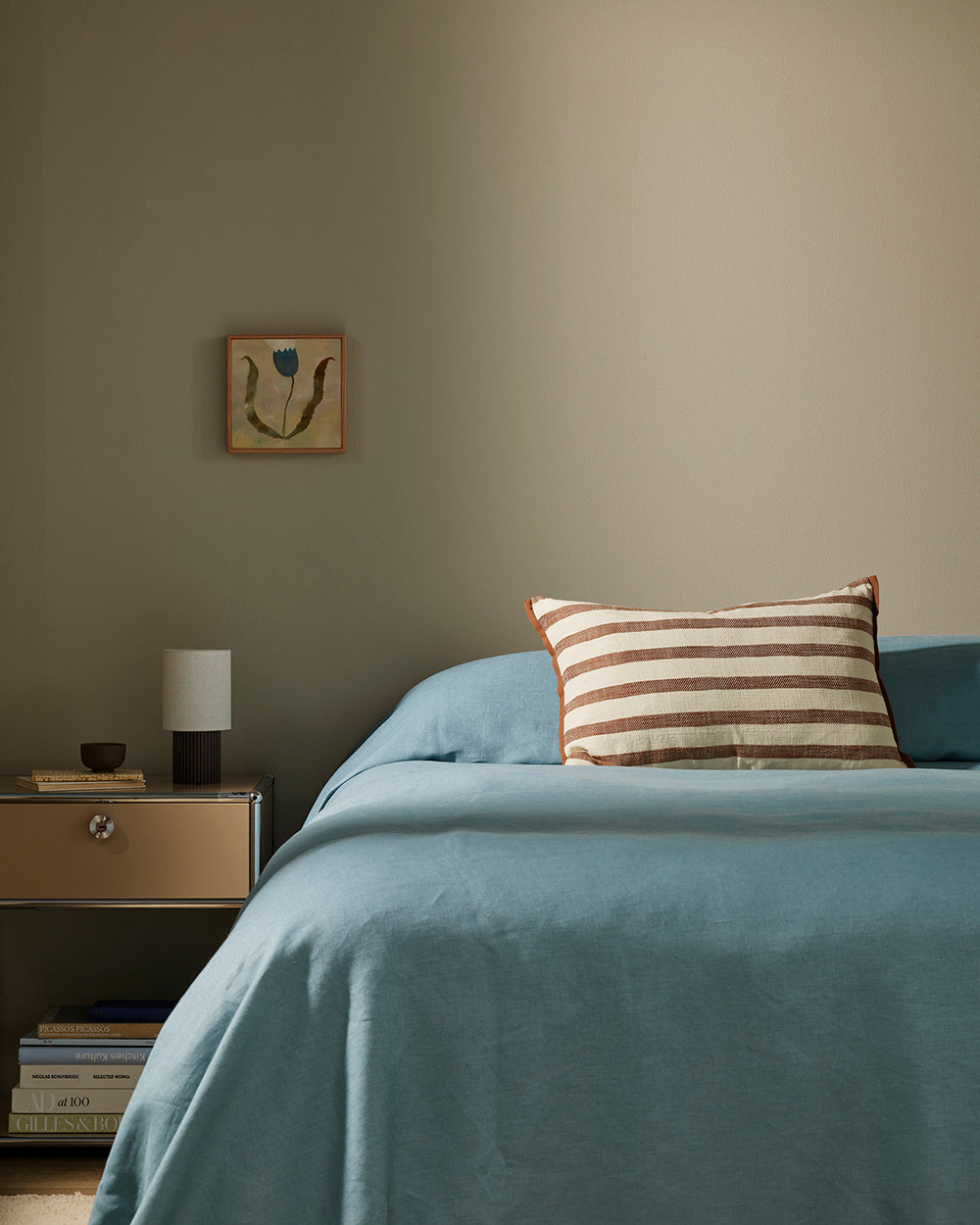 Baya Calden cotton lumbar cushion in Chestnut, styled on a bed with blue linen