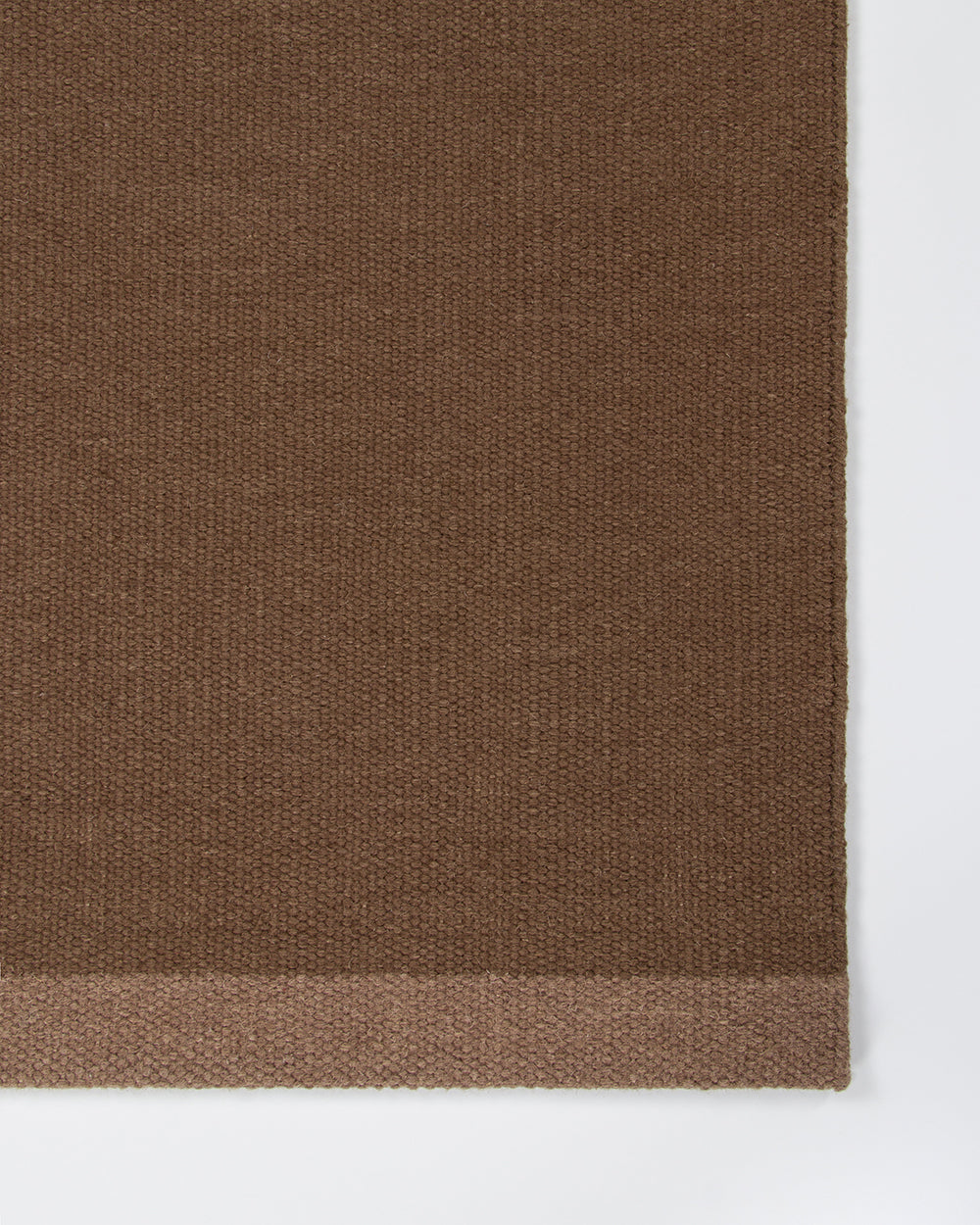 Baya Carla NZ wool floor mat in Cocoa, close view of the woven texture and the lighter brown end band.