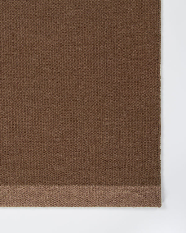 Baya Carla NZ wool floor mat in Cocoa, close view of the woven texture and the lighter brown end band.