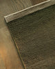 Baya Carla NZ wool floor mat in Military, folded corner showing the weave and underside on a wood floor.