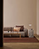 Baya Cortile lumbar cushion in Multi styled in a living room on a grey sofa, with a marble side table, table lamp and terracotta rug.
