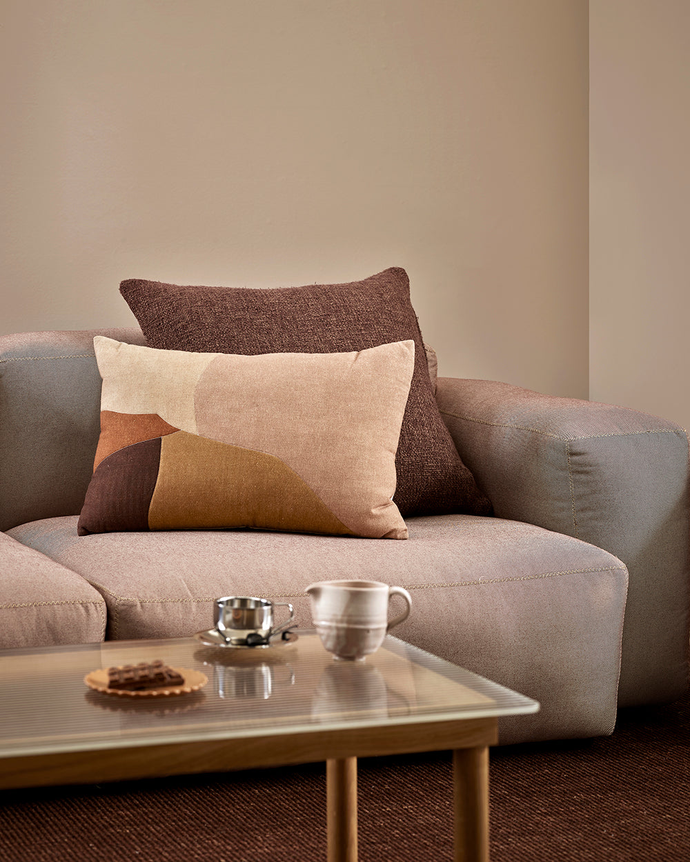 Baya Cortile lumbar cushion in Multi styled on a grey sofa with a solid brown cushion, beside a coffee setting on a glass and timber coffee table.
