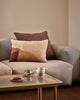 Baya Cortile lumbar cushion in Multi styled on a grey sofa with a solid brown cushion, beside a coffee setting on a glass and timber coffee table.