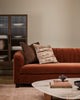 Baya Dover Chocolate cushion styled on a rust velvet sofa with a patterned cushion, in front of a ribbed glass cabinet