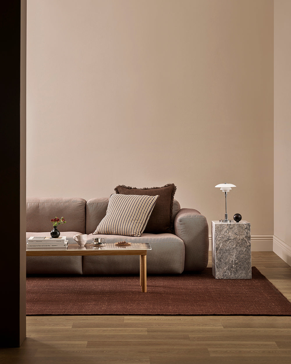 Wider view of the Baya Dover Chocolate cushion styled on a grey sofa in a living room setting