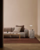 Wider view of the Baya Dover Chocolate cushion styled on a grey sofa in a living room setting