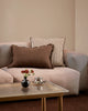 Baya Dover Chocolate lumbar cushion styled on a grey sofa alongside a striped cushion, close view with a vase of flowers on the coffee table