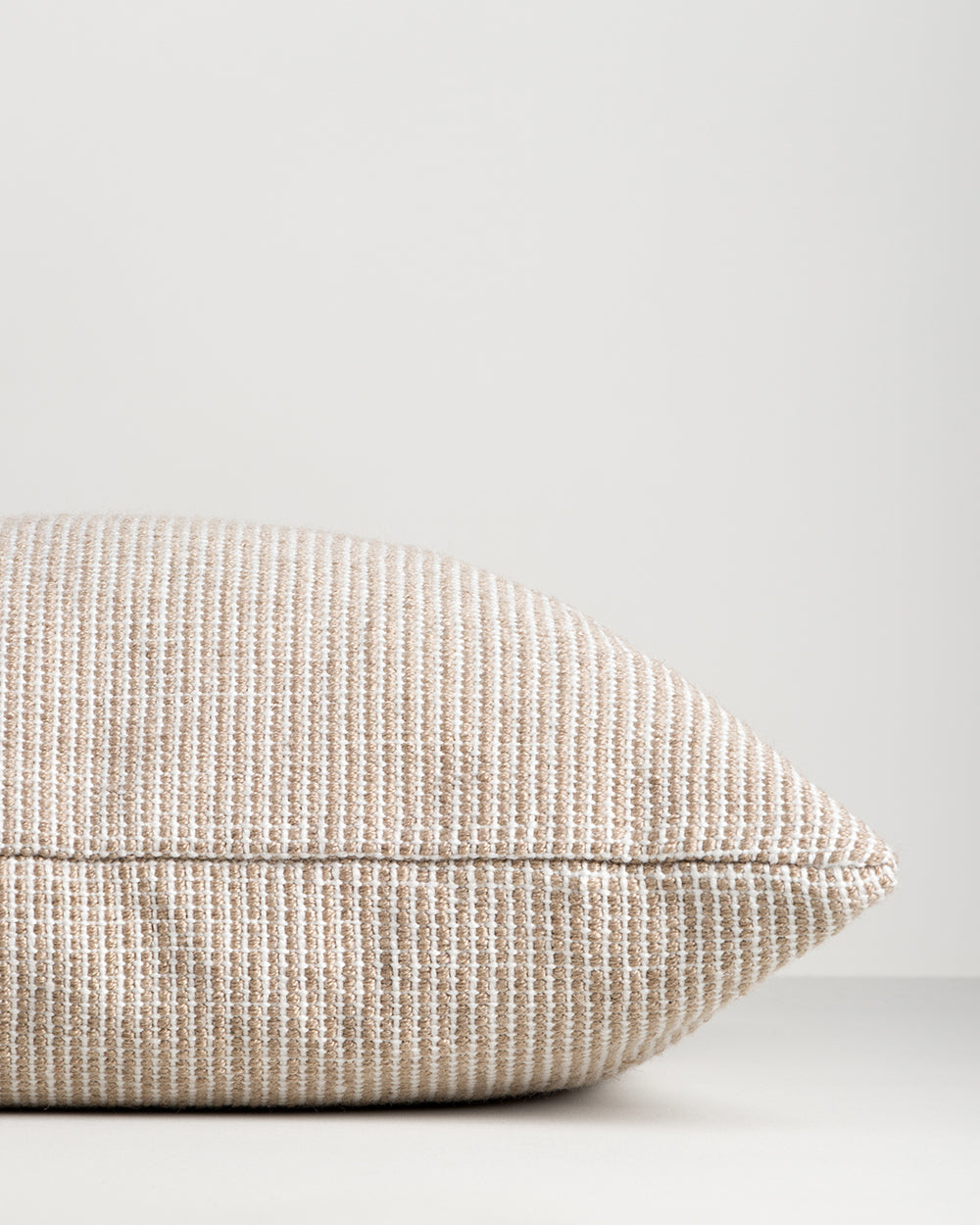 Side profile of the Baya Dune outdoor cushion in Almond, lying flat, showing the piped seam edge