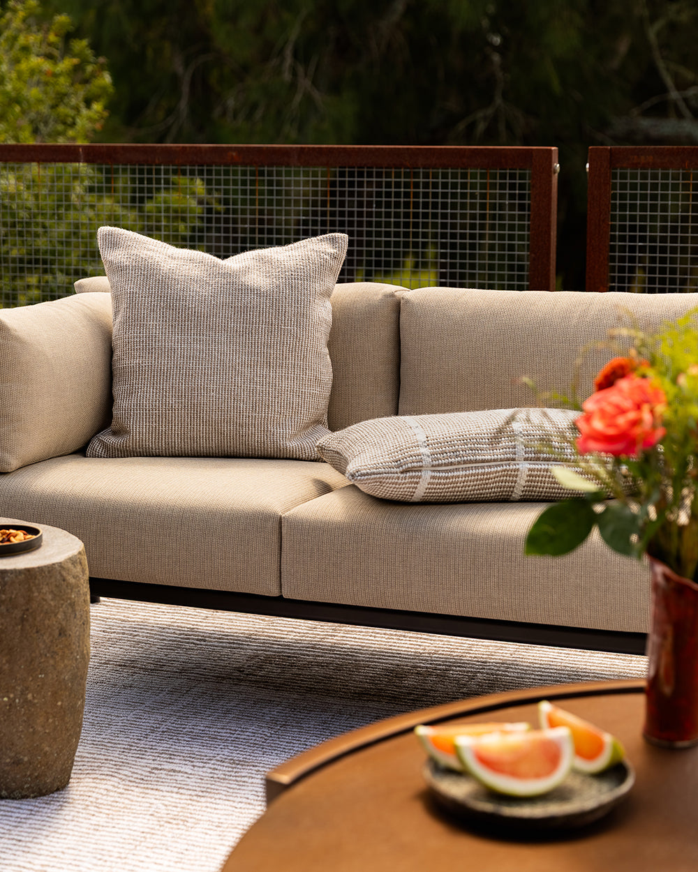 Baya Dune outdoor cushion in Almond styled on an outdoor sofa setting, wider view of the deck