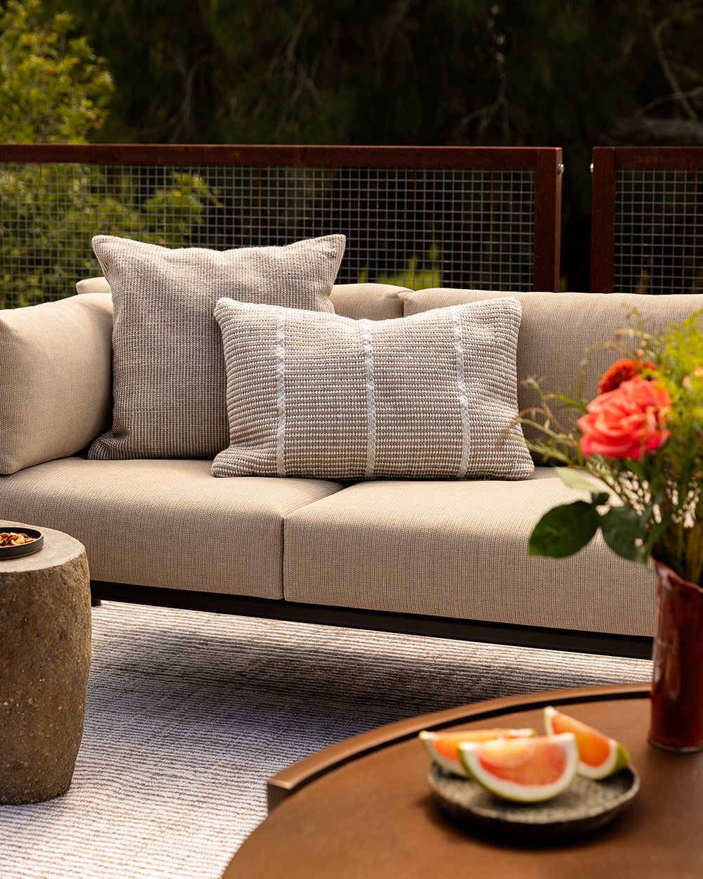 Baya Dune outdoor cushion in Almond styled on an outdoor sofa with a striped lumbar cushion