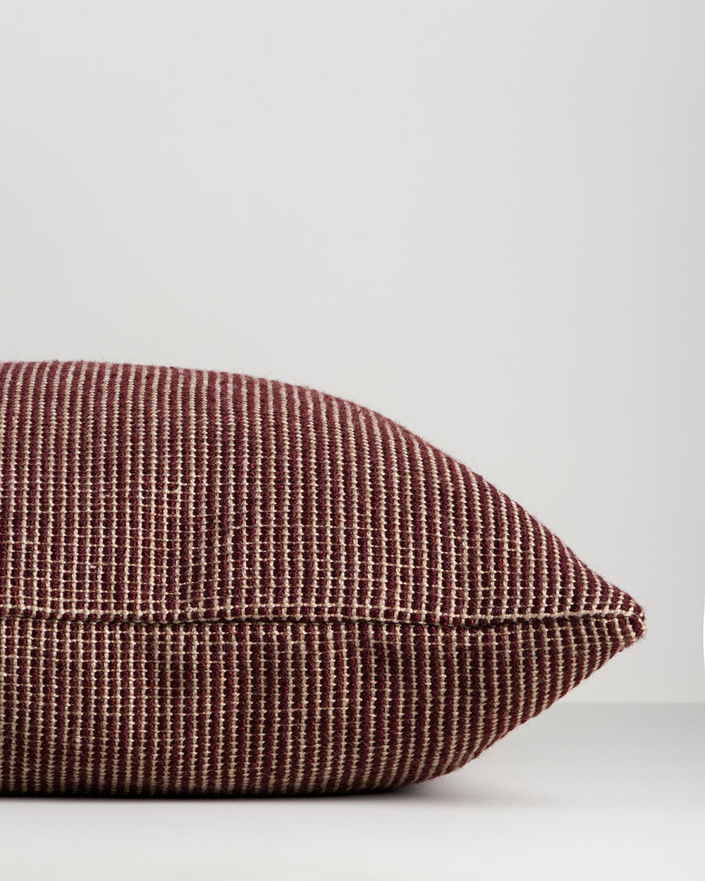 Side profile of the Baya Dune outdoor cushion in Claret, lying flat, showing the piped seam edge