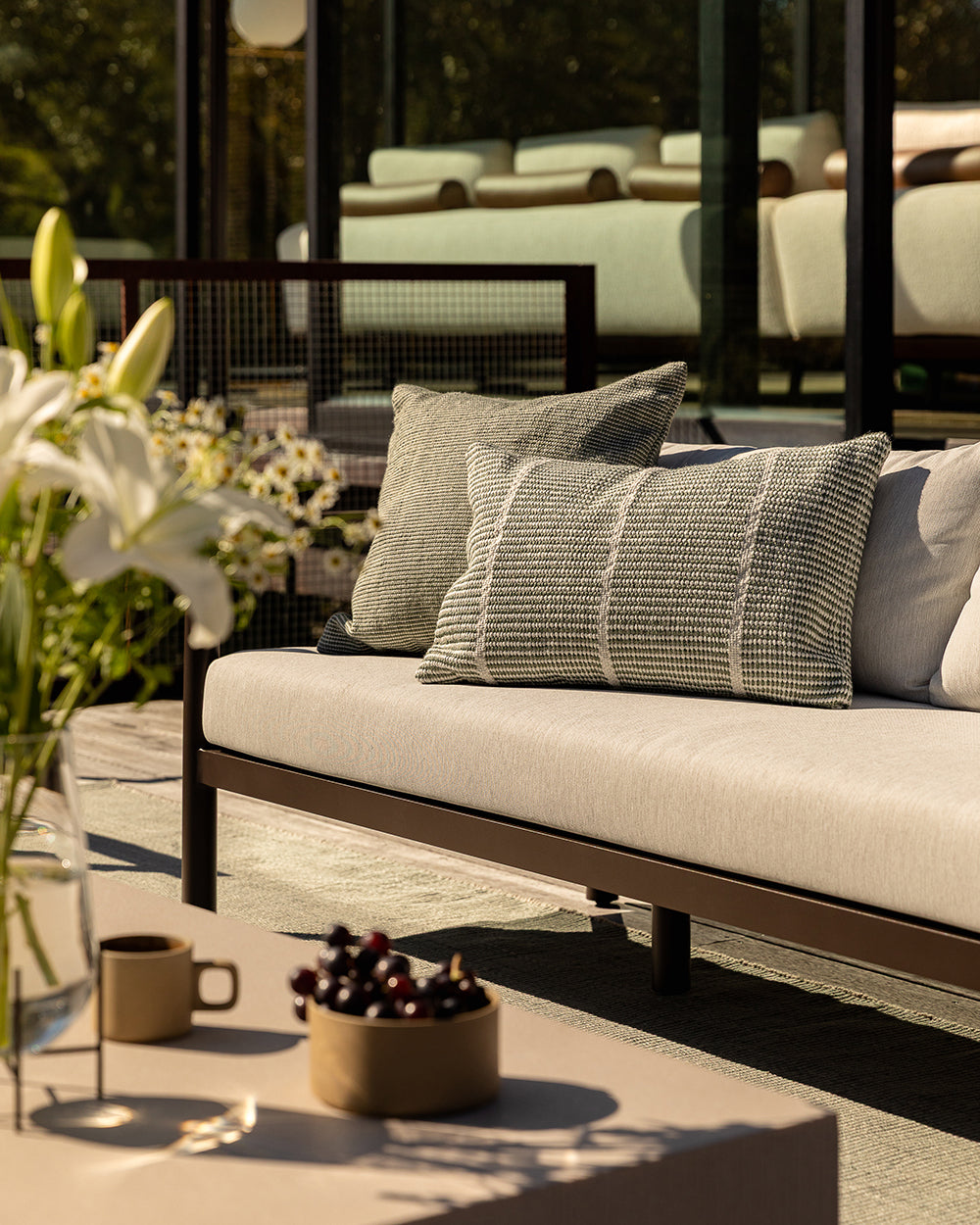Baya Dune outdoor cushion in Eucalyptus styled on an outdoor sofa with a striped lumbar cushion