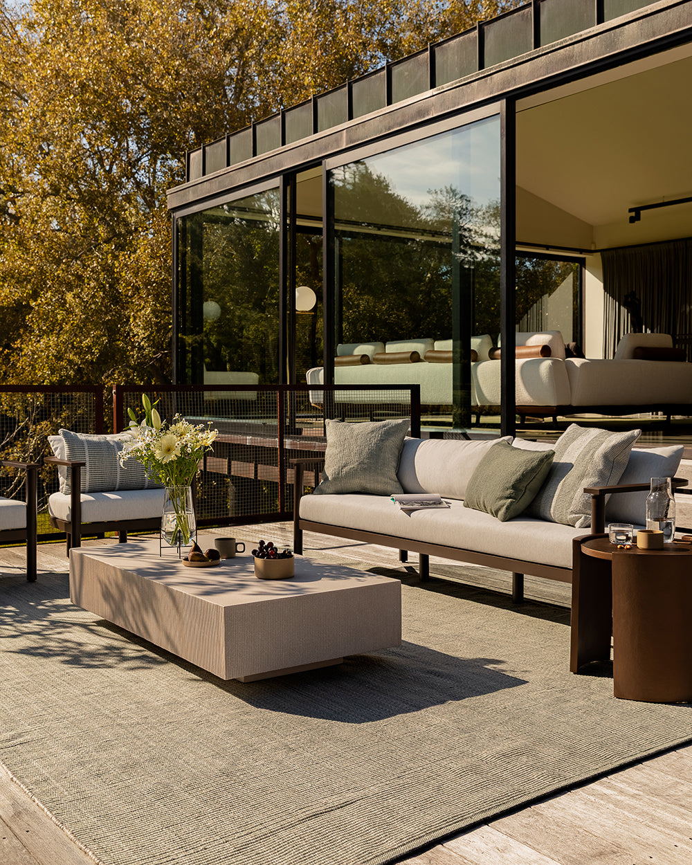 Baya Dune outdoor cushion in Eucalyptus styled on an outdoor deck setting, wide view of the sofa and armchair