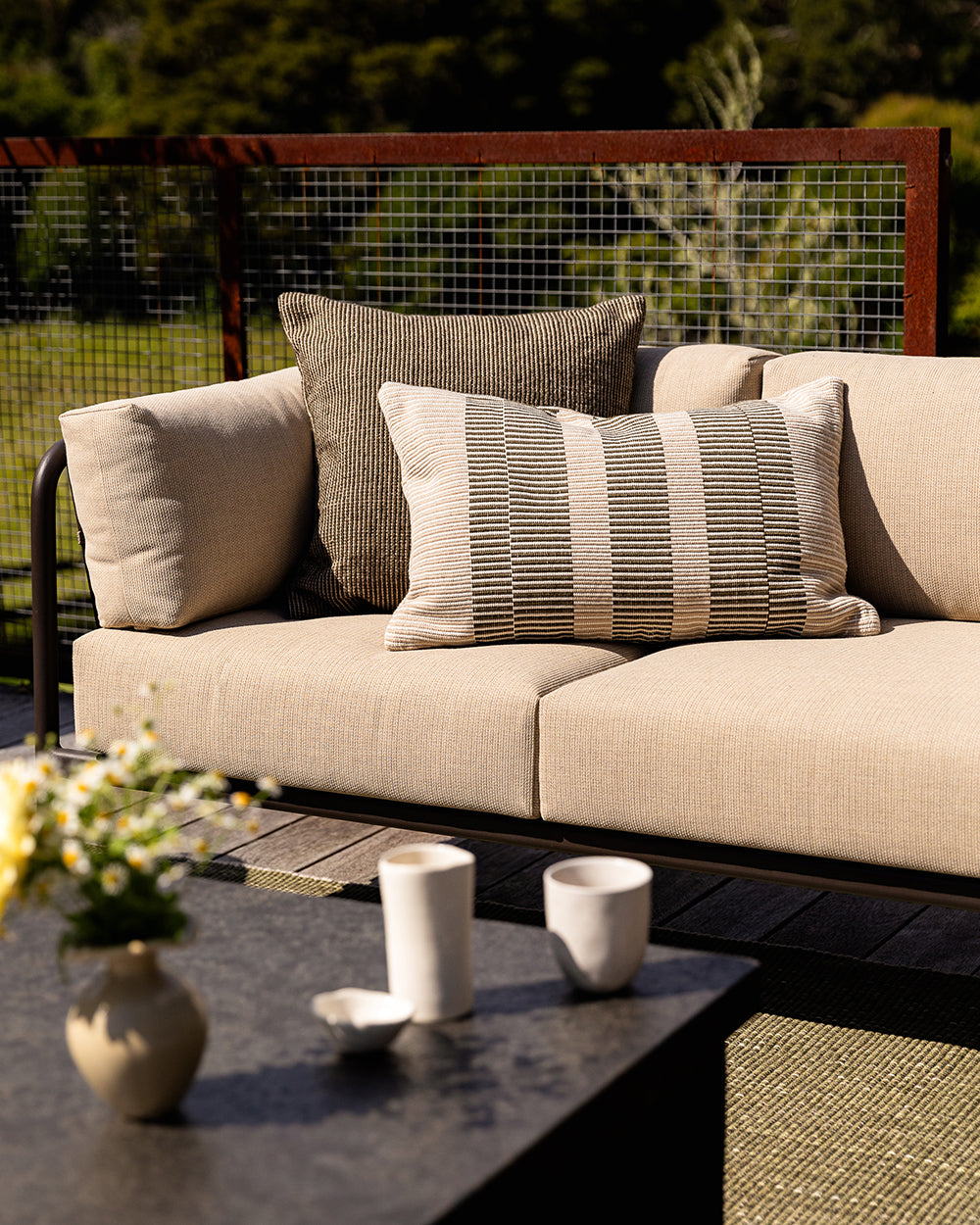 Baya Dune outdoor cushion in Mangrove styled on an outdoor sofa with a striped lumbar cushion
