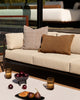 Baya Dune outdoor cushion in Tobacco styled on an outdoor sofa beside a solid rust-brown lumbar cushion, with a styled coffee table setting