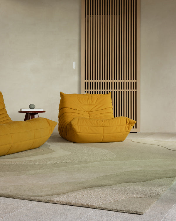 Baya Edgewater NZ wool floor rug in Pistachio, rectangle, styled in a room with two mustard lounge chairs and a slatted timber screen.