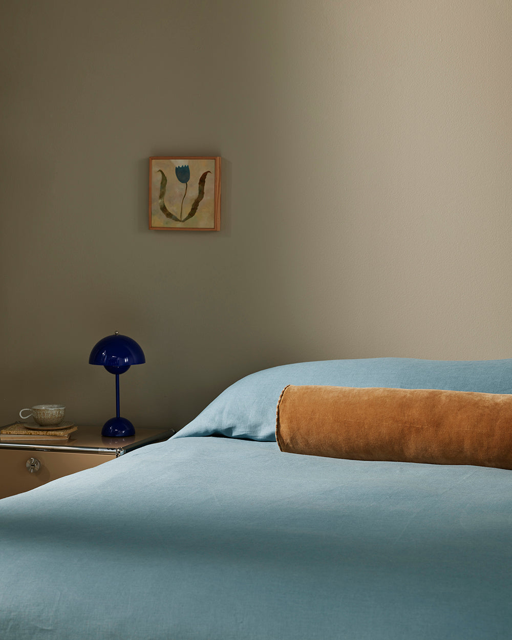 Baya Elliot cotton velvet bolster cushion in Butterscotch, close view on a bed with blue linen bedding