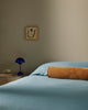 Baya Elliot cotton velvet bolster cushion in Butterscotch, close view on a bed with blue linen bedding
