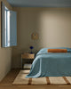 Baya Elliot cotton velvet bolster cushion in Butterscotch, on a bed in a bedroom with an open window