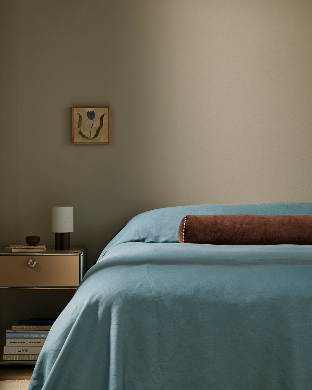 Baya Elliot cotton velvet bolster cushion in Chocolate, close view on a bed with blue linen bedding
