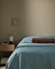 Baya Elliot cotton velvet bolster cushion in Chocolate, close view on a bed with blue linen bedding