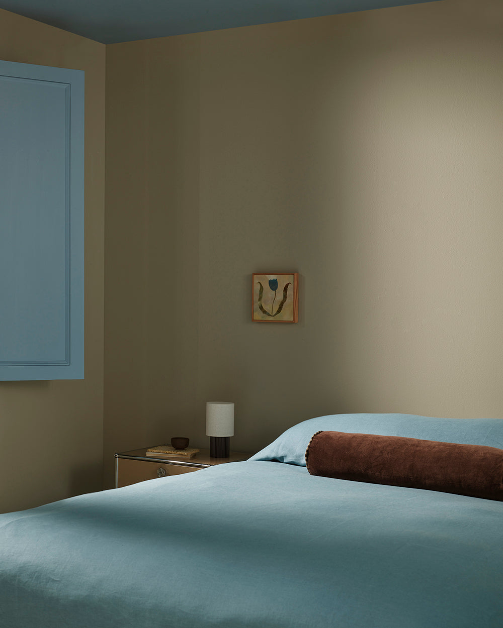 Baya Elliot cotton velvet bolster cushion in Chocolate, on a bed in a styled bedroom corner