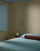 Baya Elliot cotton velvet bolster cushion in Chocolate, on a bed in a styled bedroom corner