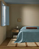 Baya Elliot cotton velvet bolster cushion in Chocolate, on a bed in a bedroom with an open window