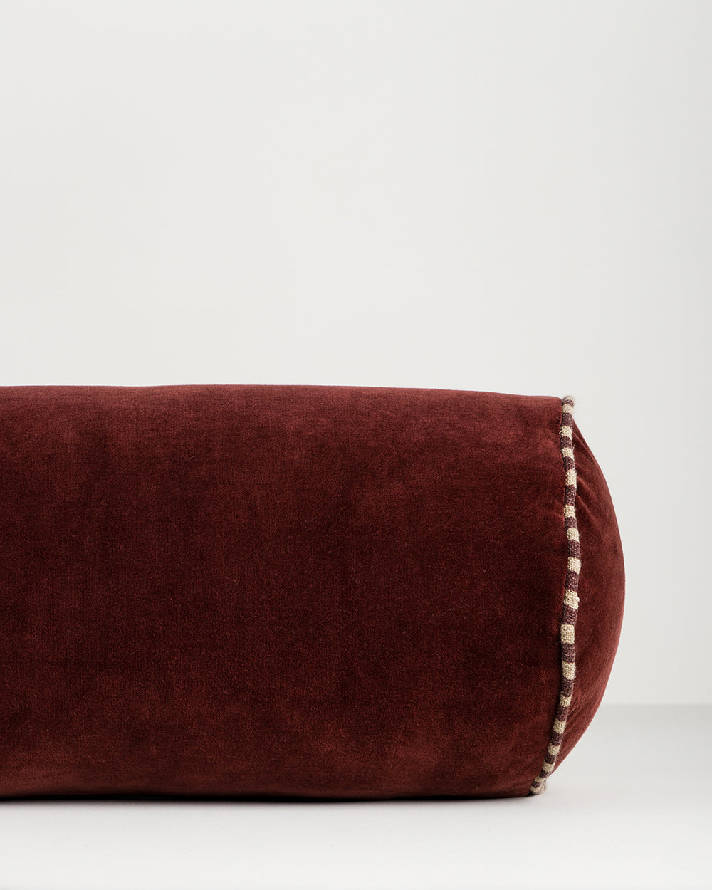 Baya Elliot cotton velvet bolster cushion in Oxblood, close view of the velvet texture and striped piped end