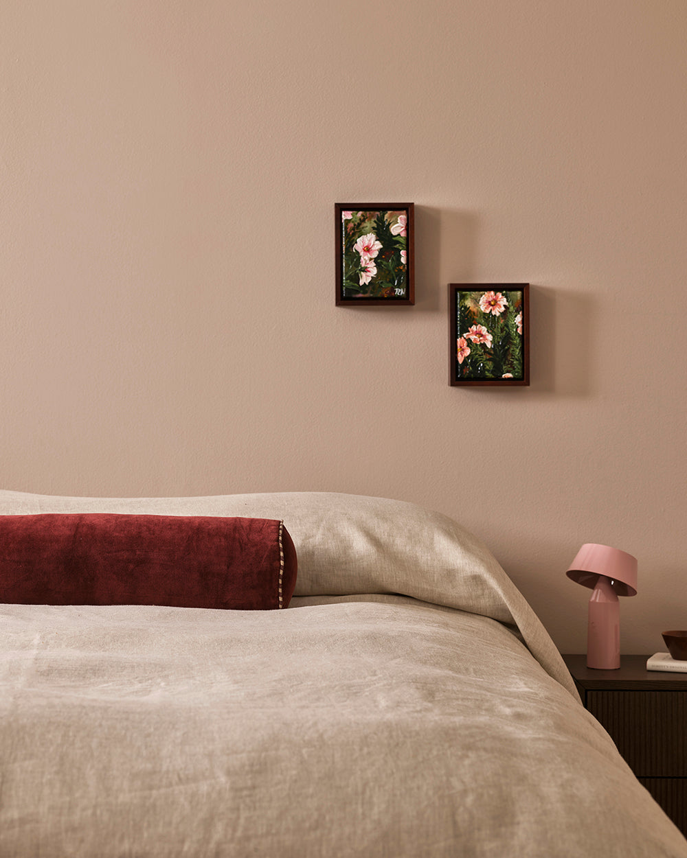 Baya Elliot cotton velvet bolster cushion in Oxblood, on a bed styled with framed botanical art