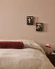 Baya Elliot cotton velvet bolster cushion in Oxblood, on a bed styled with framed botanical art