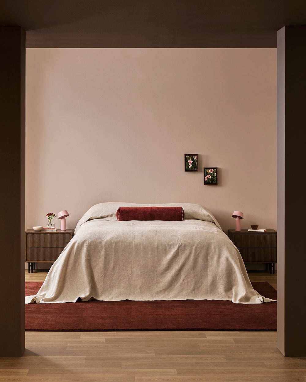 Baya Elliot cotton velvet bolster cushion in Oxblood, on a bed in a styled bedroom, wider view